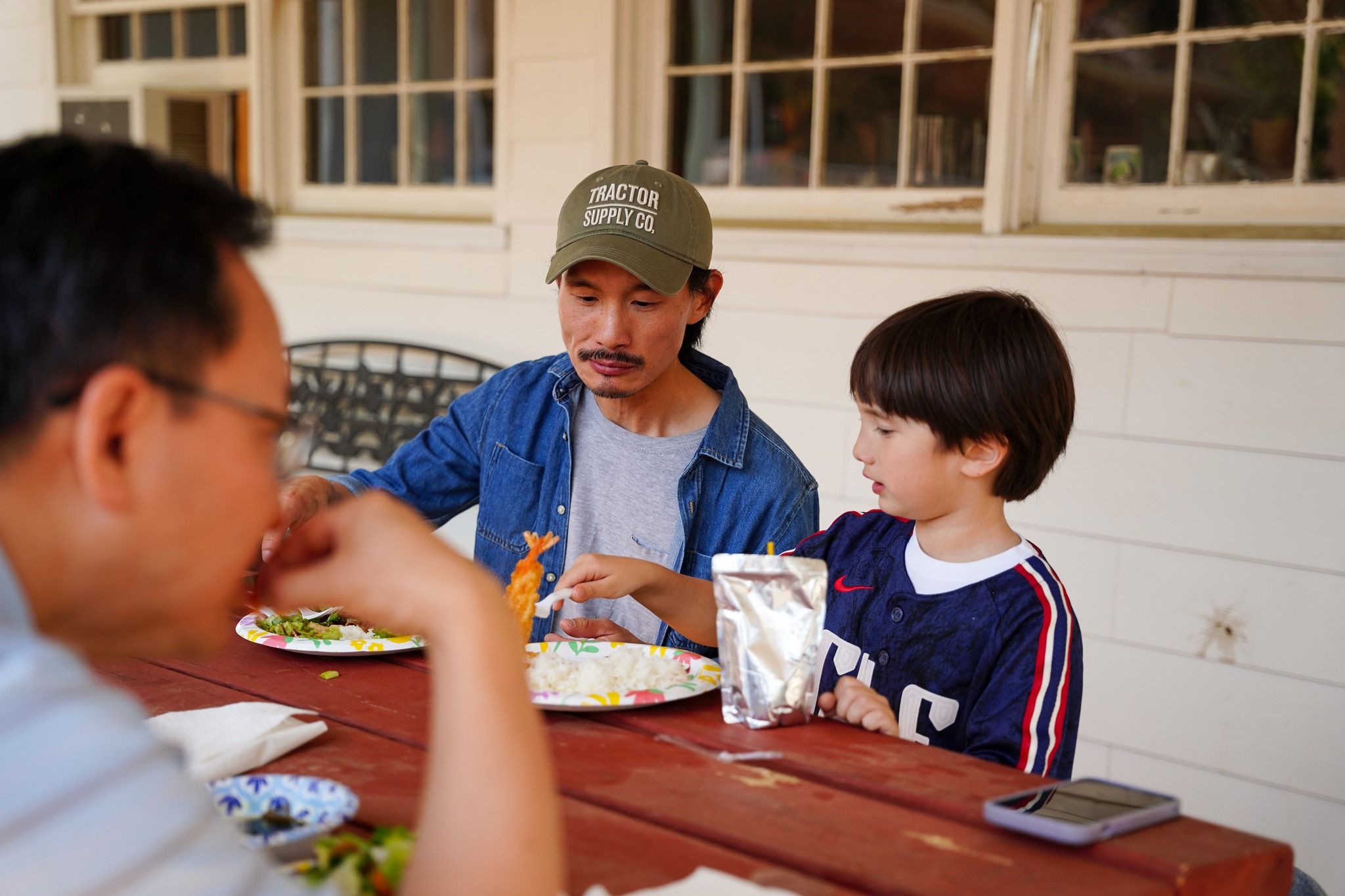 A man and a boy sharing lunch at a picnic table on the porch